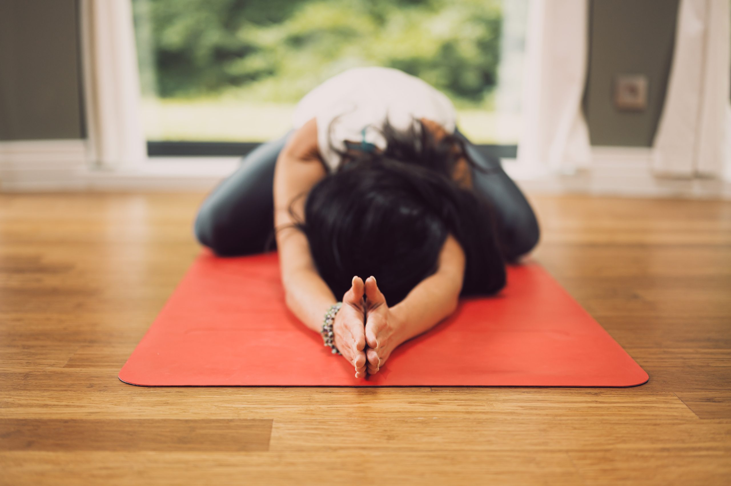 woman with dark long hair in child's pose on a red yoga mat