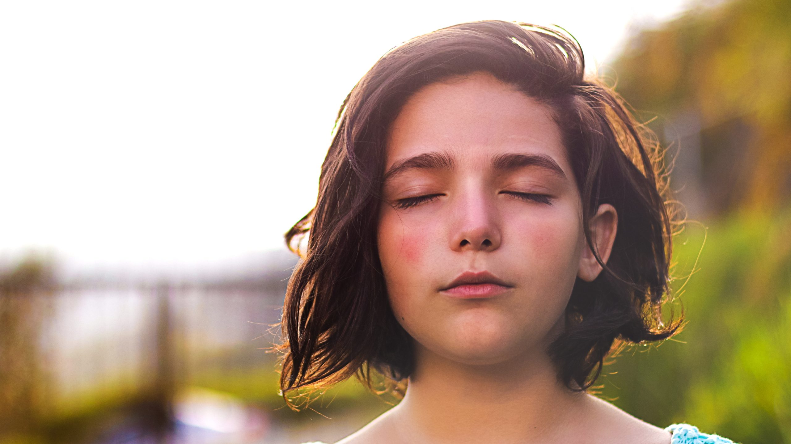 young girl with short brown hair, outside with eyes closed looking peaceful